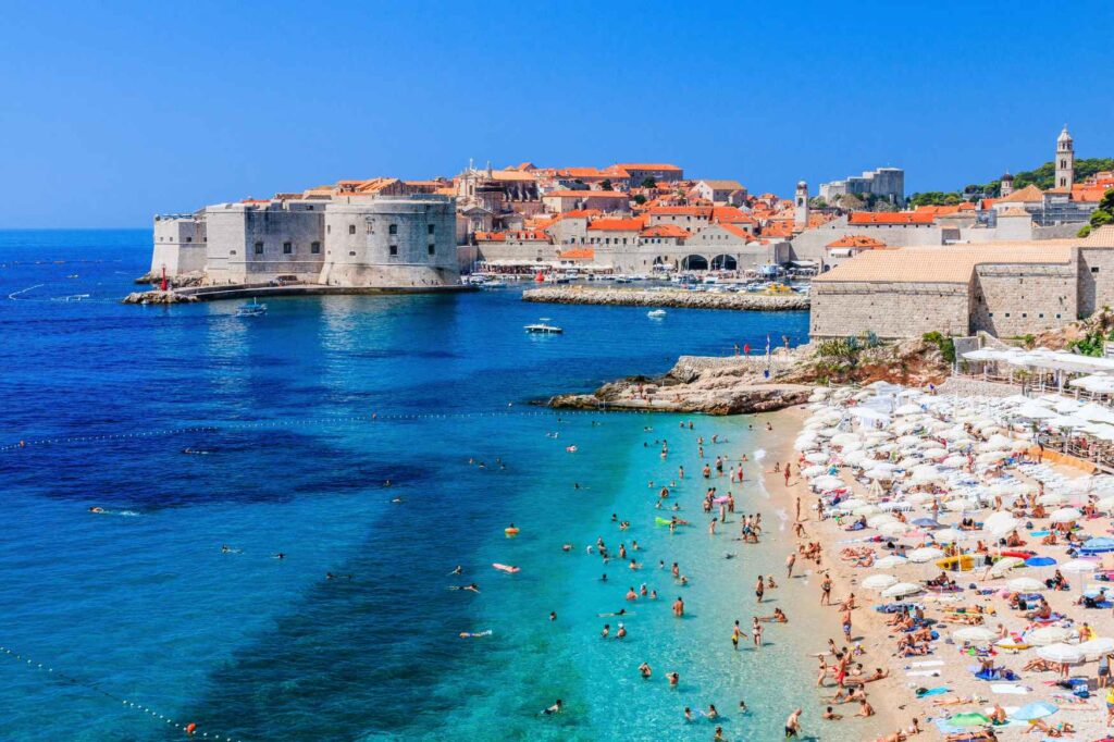 Práce v Chorvatsku – sezónní práce u moře. Pláž u Dubrovníku s historickým centrem města v pozadí